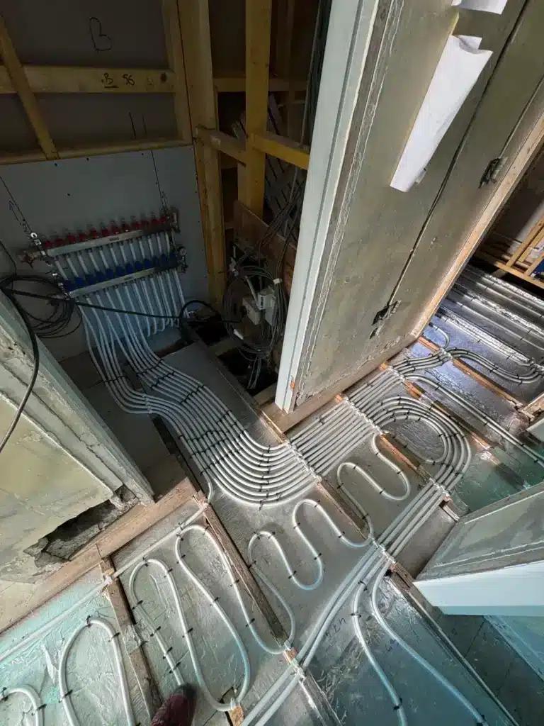 joisted floor with underfloor heating pipes staples to insulation between the joists. Pipes leading to manifold installed on the wall.